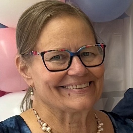 Image of woman smiling. She is wearing colorful square-framed glasses and matching beaded necklace and earrings.