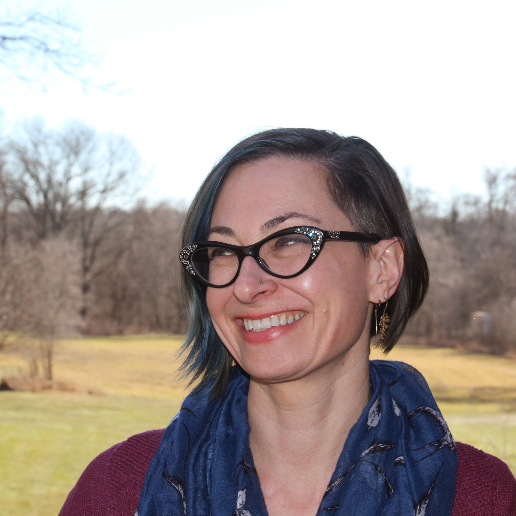Photo of woman smiling with a line of trees behind her.