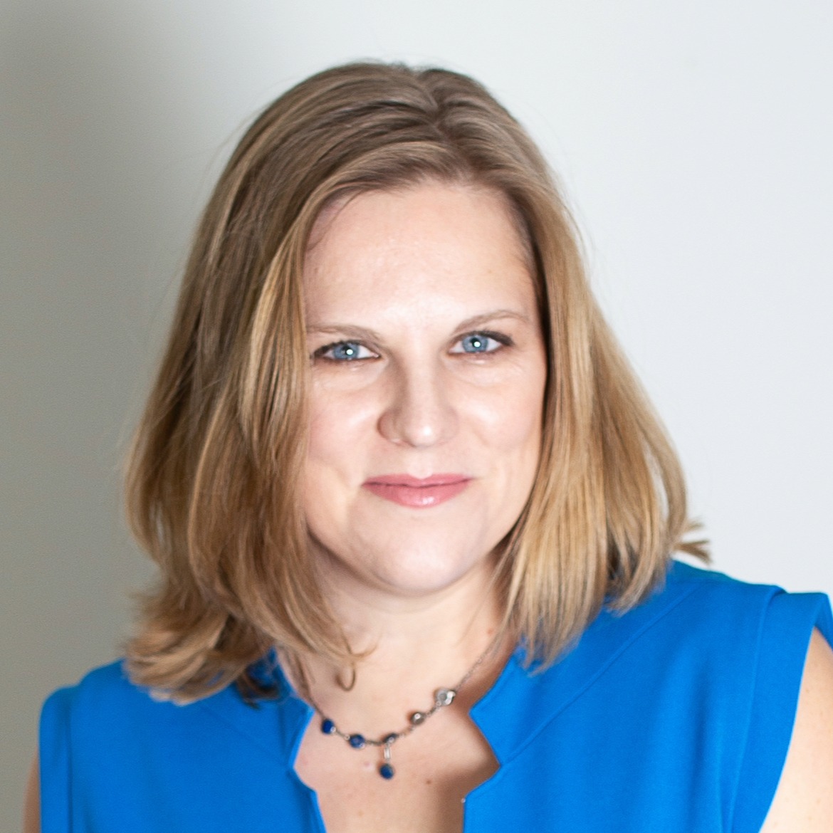 Headshot of woman smiling. She is wearing a blue shirt and a beaded necklace.
