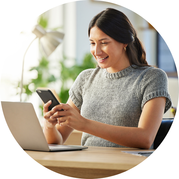 young female using her cell phone while looking at her laptop