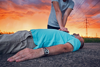 Man performing CPR on man lying on ground with storm and sunset in sky