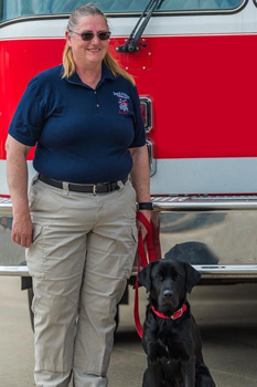 Woman standing with black labrador retriever in front of fire truck