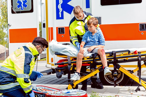 Child sits on gurney outside ambulance as EMS workers treat his injuries