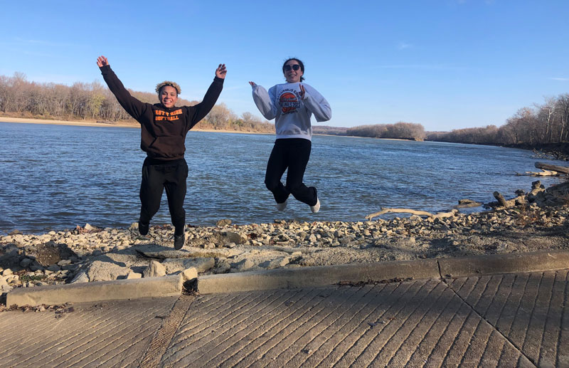 Two people jumping in front of lake