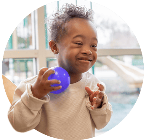 Young child with Downs Syndrome smiling while playing with a ball.