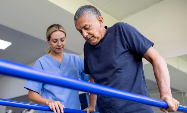 Nurse assisting man walking using parallel bars.