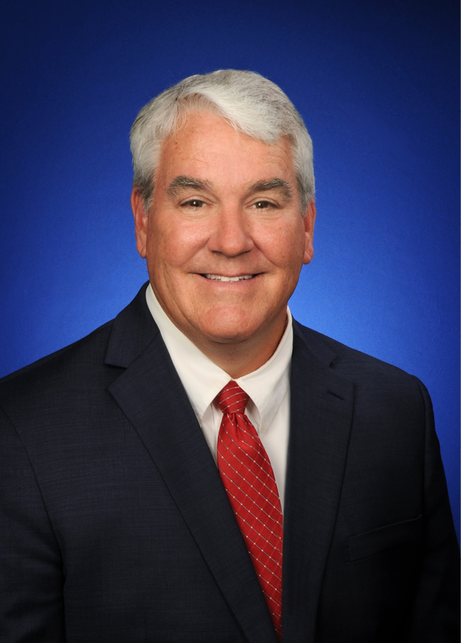 <img alt="A photo of IURC Commissioner Andy Zay, dressed in a black suit with a red tie against a blue background." />