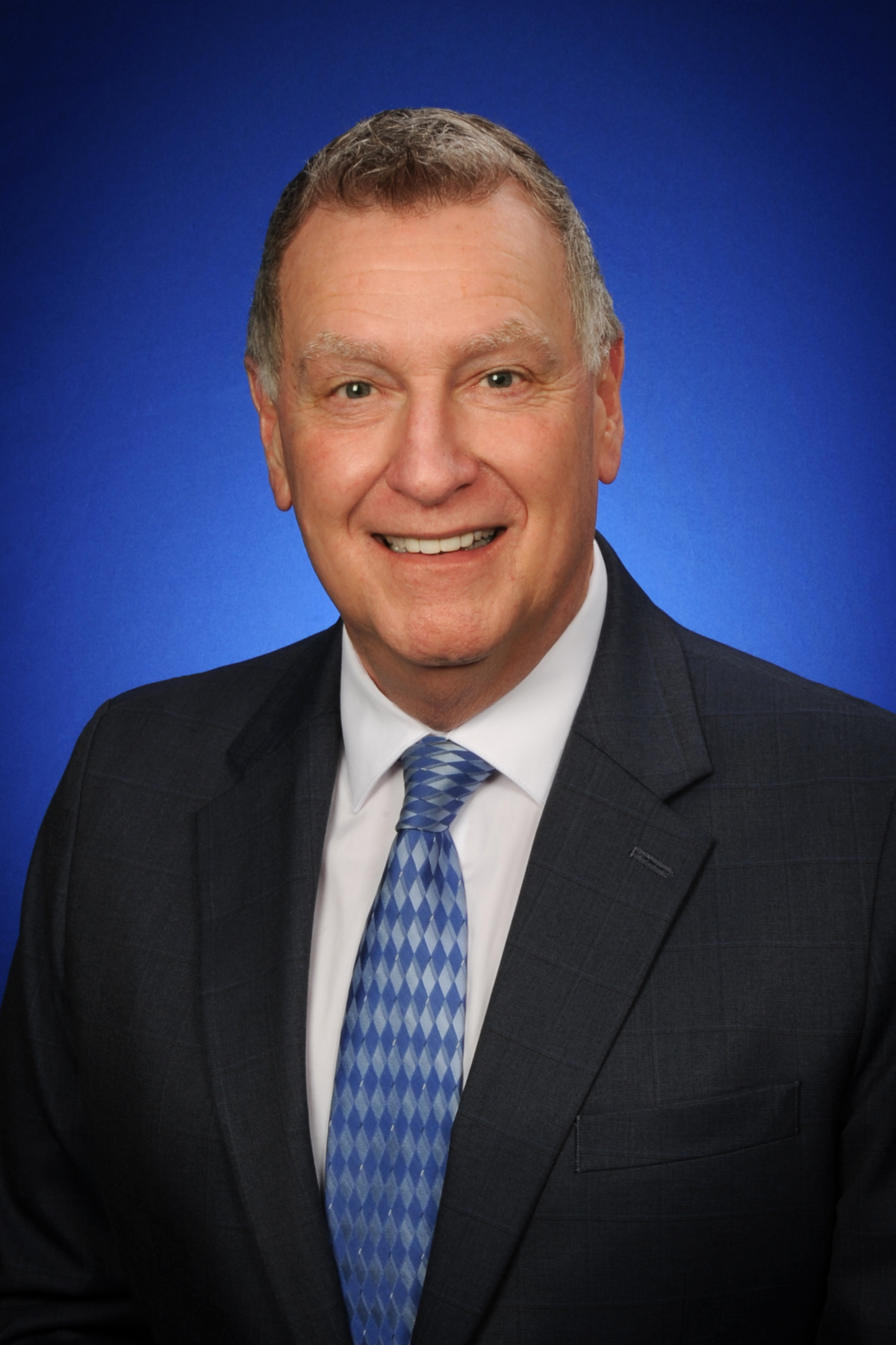 Commissioner Deig Commissioner Deig is a blue suit with a light blue tie against a bright blue background