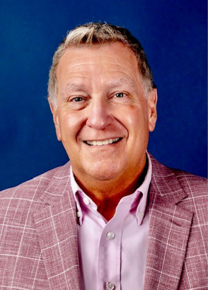 <img alt="A photo of IURC Commissioner Bob Deig, dressed in a pink suit, against a dark blue background." />