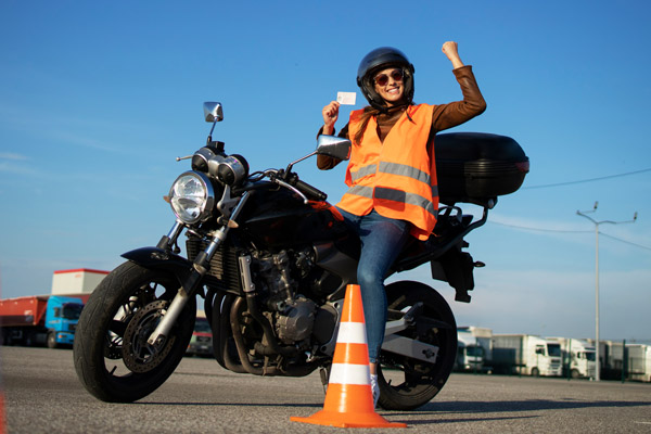 Young woman sitting on a motorcycle holding up her license with a smile on her face.