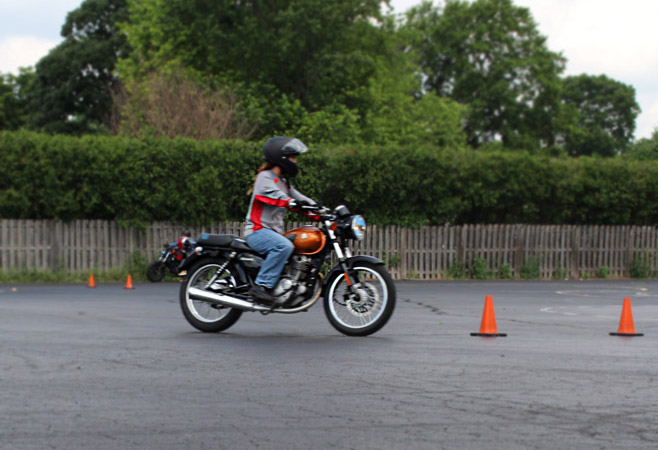 Female motorcycle trainee learning to weave between cones.